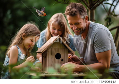 Man and two young girls assemble a birdhouse outdoors as a bird flies nearby Man and two young girls assemble a birdhouse outdoors as a bird flies nearby 112506448