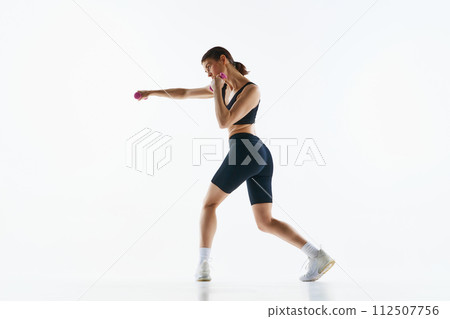 Young woman with slim sportive body training, doing jab exercises with dumbbells isolated over white studio background Young woman with slim sportive body training, doing jab exercises with dumbbells isolated over white studio background 112507756