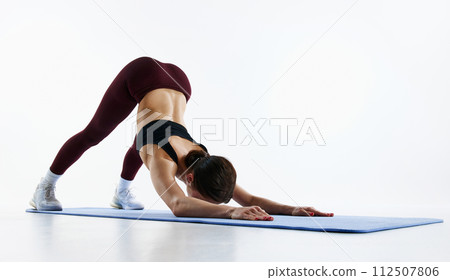 Young woman with slim, fit, healthy body training, doing yoga exercises, standing in extended puppy pose isolated over white studio background 112507806