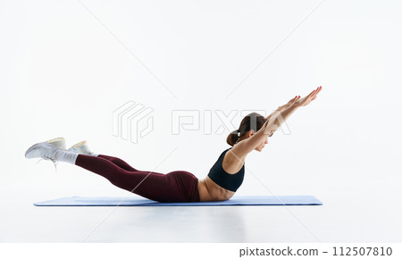 Young slim woman taking care after body condition, doing yoga exercises, standing in bow pose isolated over white background 112507810