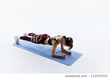 Young sportive girl with fit, slim body training on fitness mat, standing in plank position isolated over white studio background Young sportive girl with fit, slim body training on fitness mat, standing in plank position isolated over white studio background 112507814