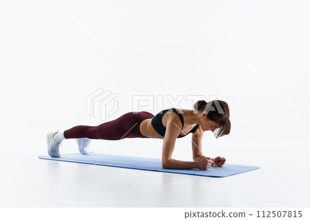 Young sportive girl with fit, slim body training on fitness mat, standing in plank position isolated over white studio background 112507815