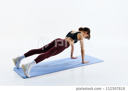 Sportive young woman in sportswear, with fit body training on fitness mat, standing in plank position isolated over white studio background 112507818
