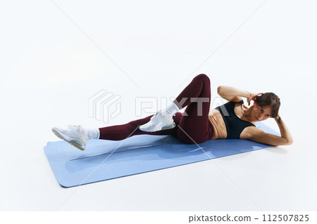 Sportive young woman in sportswear, leggings and top training in fitness mat, doing bicycle crunch exercises isolated over white studio background 112507825