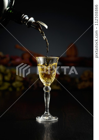 Yellow herbal liquor is poured from a vintage bottle into a glass. Yellow herbal liquor is poured from a vintage bottle into a glass. 112508866