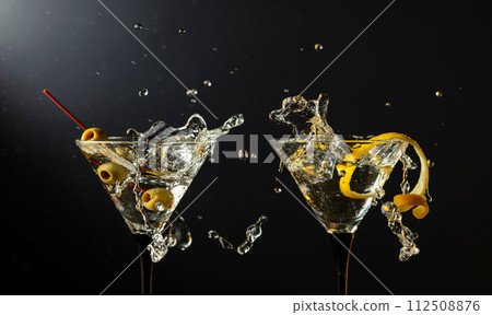 Classic dry martini cocktails with green olives and lemon peel on a black background. Classic dry martini cocktails with green olives and lemon peel on a black background. 112508876