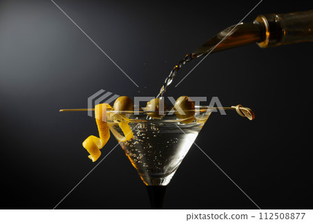 Classic dry martini cocktail with green olives and lemon peel on a black background. 112508877