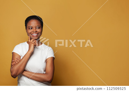 Beautiful thinking African American woman in white t-shirt standing on colorful yellow background Beautiful thinking African American woman in white t-shirt standing on colorful yellow background 112509325