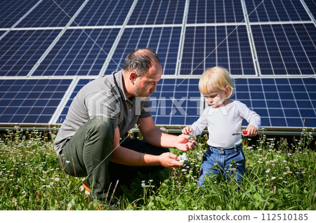 Father showing to his little son how to use tools in background of solar panels. Dad teaching his child how to use screwdriver. Cute son and father learning tools on background of solar panels. Father showing to his little son how to use tools in background of solar panels. Dad teaching his child how to use screwdriver. Cute son and father learning tools on background of solar panels. 112510185