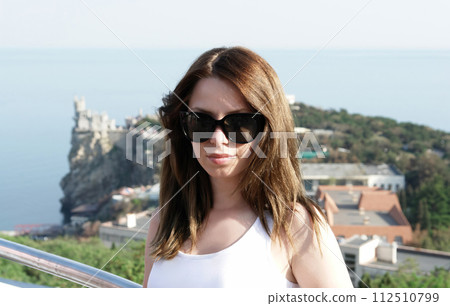 July 2012 Ukraine Crimea. Portrait of a young girl in black glasses against the backdrop of the sea and the Swallow's Nest castle. AI-generated item 112510799
