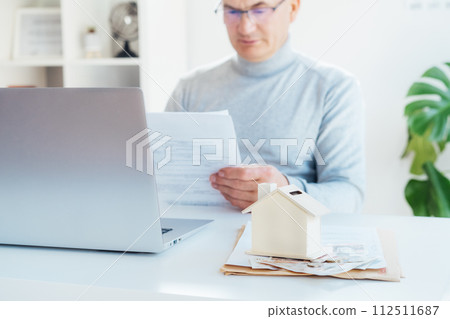 House model money box with cash on table and blurred man with docs works on laptop. Housing cost and payments. Real estate, property investment. Home mortgage loan rate. Saving money for retirement. House model money box with cash on table and blurred man with docs works on laptop. Housing cost and payments. Real estate, property investment. Home mortgage loan rate. Saving money for retirement. 112511687