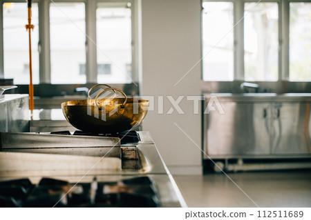 Shiny metal bowl occupies stove in a professional kitchen of a modern restaurant. Clean arrangement of chrome appliances equipment and new furniture. Bright gas service is working. 112511689
