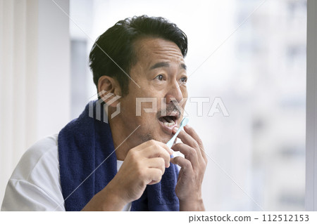 A man in his 50s worries about his gums while brushing his teeth. 112512153