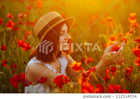 Beautiful girl in the poppy field at sunset in a white dress and hat. Beautiful girl in the poppy field at sunset in a white dress and hat. 112514554