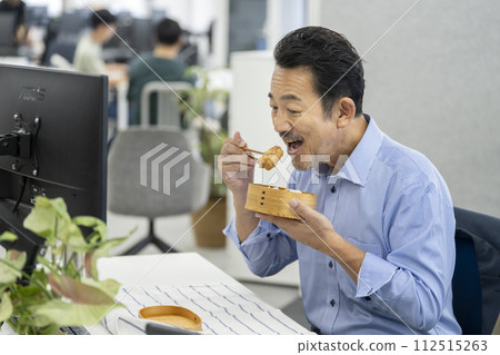 一名 50 多歲的男子在工作時吃午餐 112515263