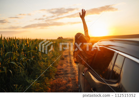 Happy woman outstretches her arms while sticking out car window. Lifestyle, travel, tourism, nature. 112515352