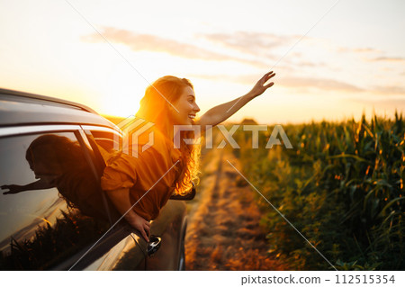 Happy woman outstretches her arms while sticking out car window. Lifestyle, travel, tourism, nature. 112515354