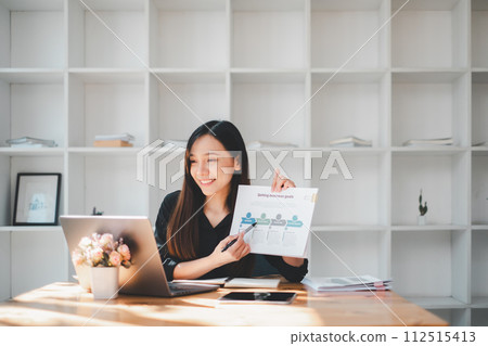 A smiling businesswoman presents a document with business goals, indicative of strategic planning and achievement in a bright, modern office. A smiling businesswoman presents a document with business goals, indicative of strategic planning and achievement in a bright, modern office. 112515413