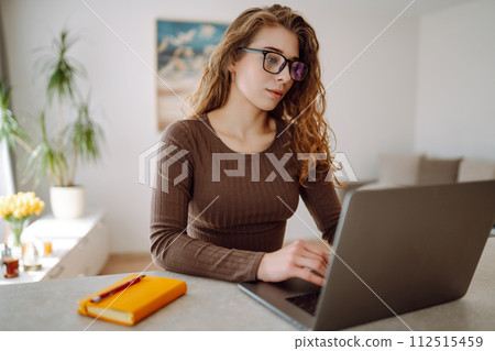 Focused young woman sits at table with laptop and bright notepad. Concept of freelancing, vacation. 112515459
