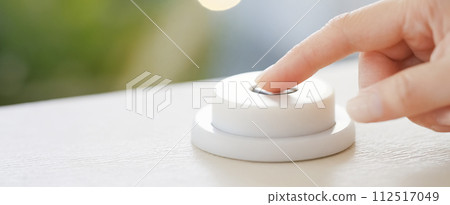Close-up of a woman's finger pressing a round switch in a bright room 112517049