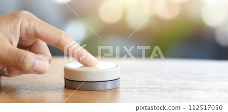 Close-up of a woman's finger pressing a round switch in a bright room 112517050