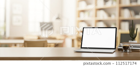 A wooden table features a laptop mockup in a cosy neutral coffee shop or library co-working space. A wooden table features a laptop mockup in a cosy neutral coffee shop or library co-working space. 112517174