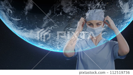 Portrait of female surgeon wearing face mask against globe on blue background 112519736