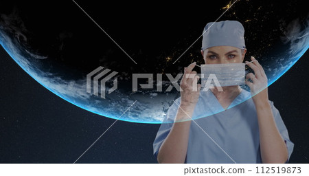 Portrait of female surgeon wearing face mask against globe on blue background 112519873