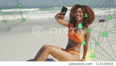 Image of networks with digital icons over woman taking selfie with smartphone on beach 112520083