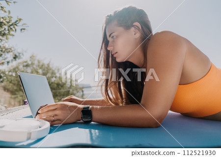 Woman laptop sea. Working remotely on seashore. Happy successful woman female freelancer working on laptop by the sea at sunset, makes a business transaction online. Freelance, remote work on vacation 112521930