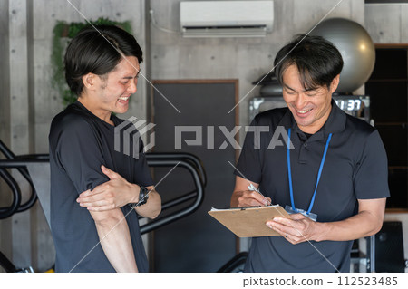 A male personal trainer listens to the concerns of male members during personal training counseling 112523485