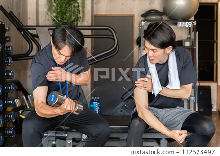 A male trainer showing training samples to members at a personal gym (arm training) A male trainer showing training samples to members at a personal gym (arm training) 112523497