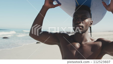 Young African American man holds a surfboard at the beach 112523607