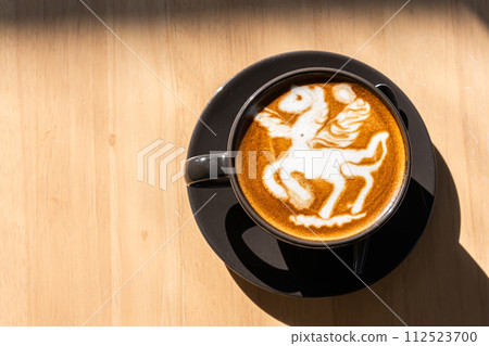 Hot coffee latte with latte art in the form of a horse milk foam in cup mug on wood desk on top view. As breakfast In a coffee shop at the cafe,during business work concept Hot coffee latte with latte art in the form of a horse milk foam in cup mug on wood desk on top view. As breakfast In a coffee shop at the cafe,during business work concept 112523700