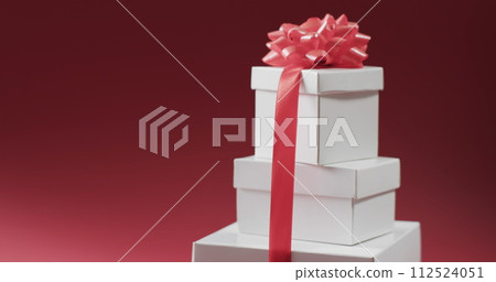 Three stacked gift boxes tied with a pink ribbon, set against a red background Three stacked gift boxes tied with a pink ribbon, set against a red background 112524051