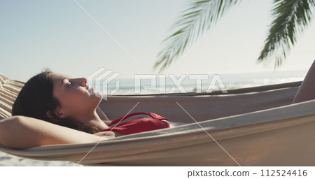 Young Caucasian woman relaxes in a hammock by the beach Young Caucasian woman relaxes in a hammock by the beach 112524416