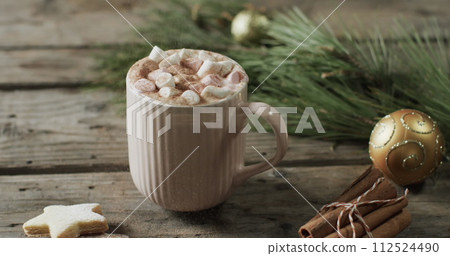 A mug of hot chocolate topped with marshmallows sits on a wooden table 112524490