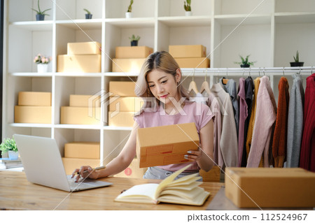Online shopping concept, Female entrepreneur confirm order and writes address on parcel boxes. Online shopping concept, Female entrepreneur confirm order and writes address on parcel boxes. 112524967