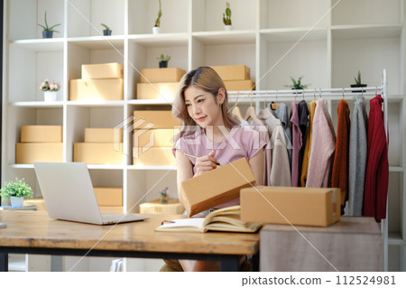 Online shopping concept, Female entrepreneur confirm order and writes address on parcel boxes. Online shopping concept, Female entrepreneur confirm order and writes address on parcel boxes. 112524981