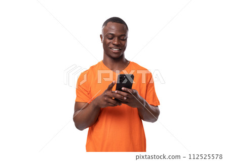young authentic african man in orange t-shirt rejoices while reading messages on smartphone young authentic african man in orange t-shirt rejoices while reading messages on smartphone 112525578