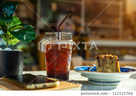 Americano iced coffee or black coffee in cup and Homemade Banana Cake, Cashew Nut Topping with smartphone on notebook on wood desk on top view In a coffee shop at the cafe,during business work concept 112525768