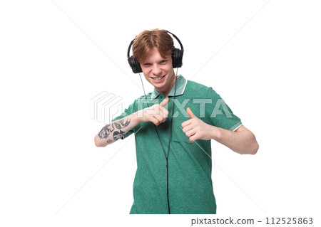 young positive red-haired caucasian guy in a green t-shirt listens to music with headphones 112525863