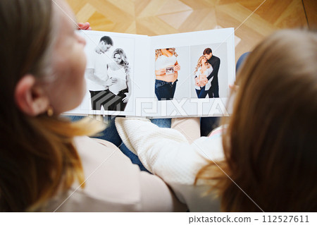 mother and daughter flips through a book with photos of dad and pregnant mom. 112527611
