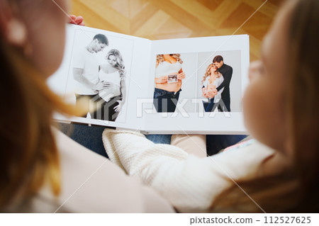 mother and daughter flips through a book with photos of dad and pregnant mom. mother and daughter flips through a book with photos of dad and pregnant mom. 112527625