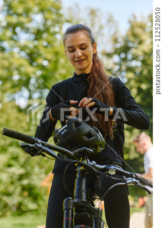 In the radiant embrace of a sunny day, a joyous girl, adorned in professional cycling gear, finds pure bliss and vitality as she cruises through the park on her bicycle, her infectious laughter 112528050