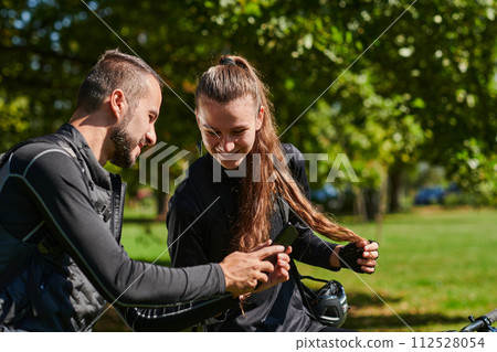 A sweet couple, equipped with bicycles and engrossed in coordinating their journey, checks their GPS mobile and watches while planning scenic routes in the park, seamlessly blending technology and A sweet couple, equipped with bicycles and engrossed in coordinating their journey, checks their GPS mobile and watches while planning scenic routes in the park, seamlessly blending technology and 112528054
