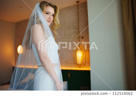 Beautiful blonde bride in white trousers, top and veil.  112528062