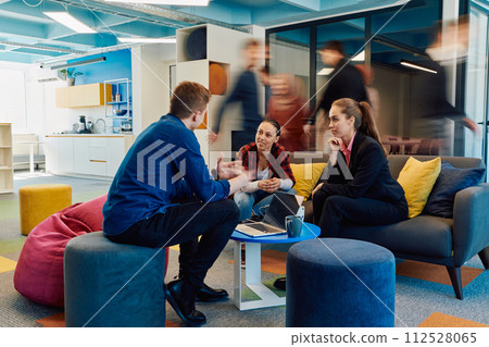 Multiethnic startup business team on meeting in a modern bright open space coworking office. Brainstorming, working on laptop. Group of coworkers walking around in motion blur 112528065