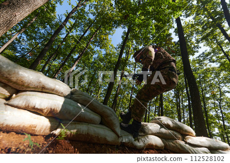 An elite soldier adeptly clears military barriers in the perilous wooded terrain, showcasing tactical skill and agility during specialized training 112528102