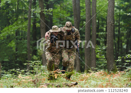 Elite soldier displays unwavering camaraderie and compassion as he aids his injured comrade, skillfully extracting him from the forest with a stretcher, showcasing the profound bond and selflessness 112528240
